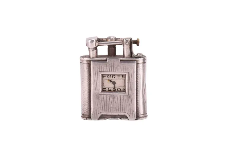 An Art Deco Dunhill silver combination lighter with novelty clock face, engine-turned case with hinged front section housing a watch with Arabic numerals