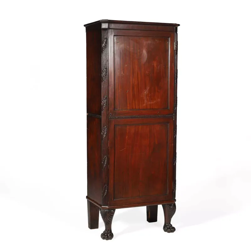 A Mahogany Side Cabinet probably Irish, of tall narrow form with two panelled doors between carved canted angles