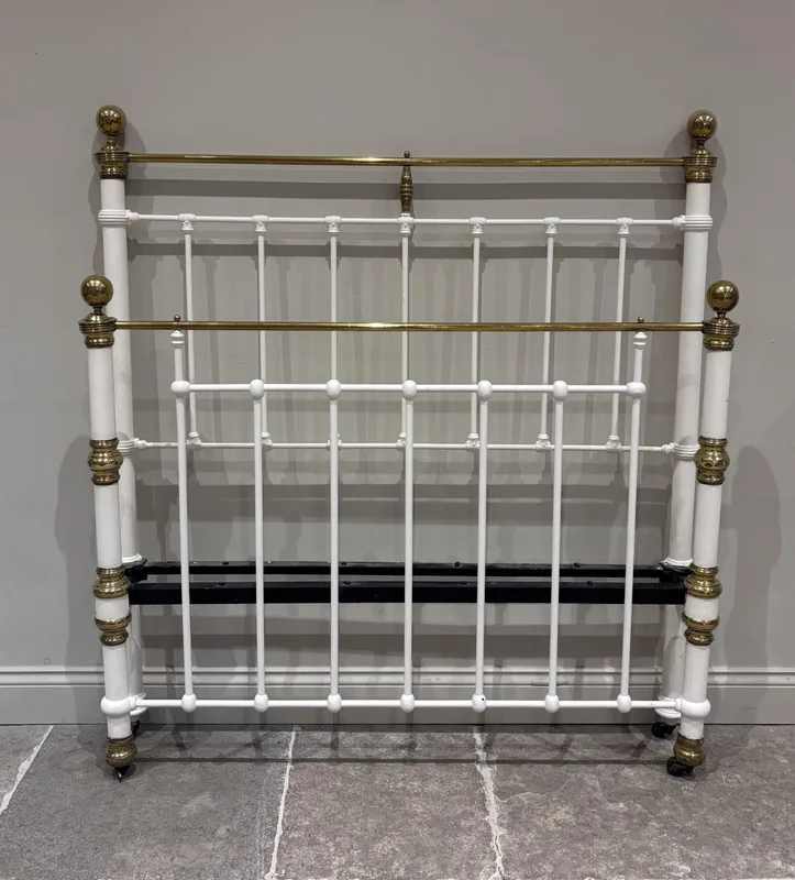 A Victorian cast iron and lacquered brass double bed frame, cream painted and raised on castors, with side irons,
