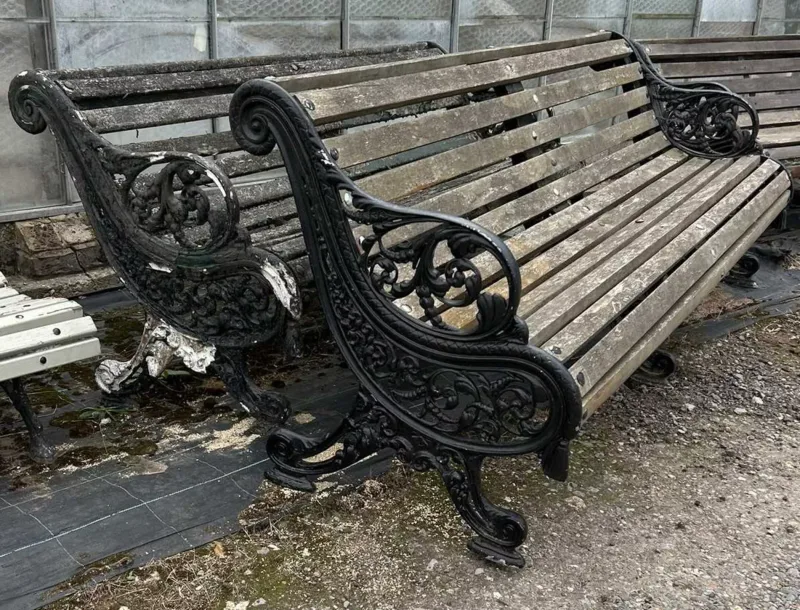 A pair of garden benches The black painted cast aluminium foliate ornamented ends with central support and teak slats to the shaped seat