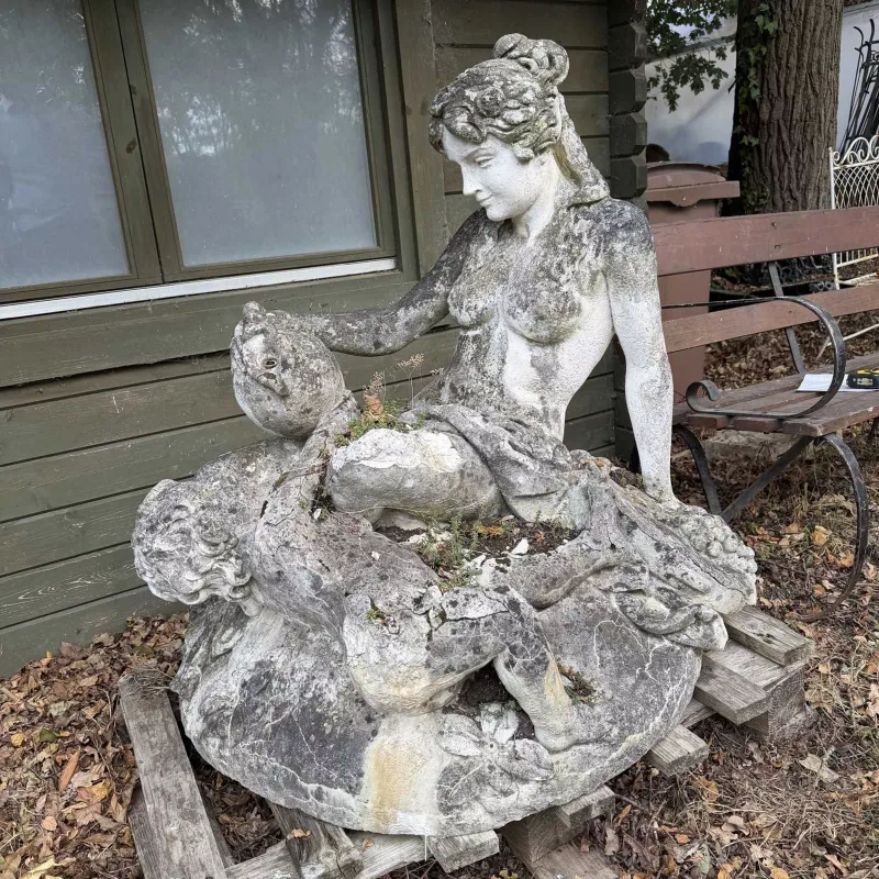 A cast reconstituted stone sculpture of a classical maiden The maiden pouring from a ewer with a putti resting at her feet