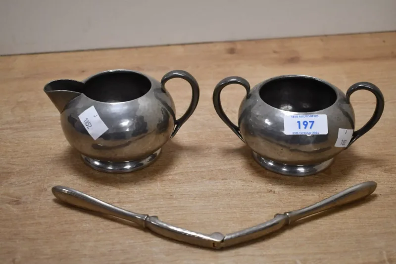An early 20th-century Art Deco Liberty & Co pewter sugar bowl and milk creamer, having a hammered pewter finish with stylised handles