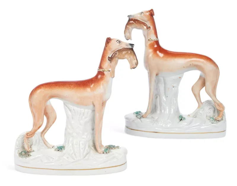 A Pair Of Staffordshire Figures Of Greyhounds 19th Century each modelled standing before a tree stump with a hare in its mouth, wearing a gilt collar