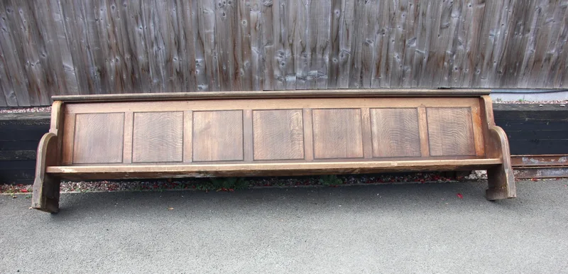 A large Victorian oak church pew, with panelled back, solid seat, and carved detail to the ends,
