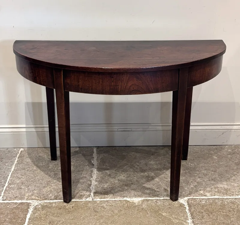 A George III mahogany D-end console table, with plain frieze and raised on four legs of tapering square section,