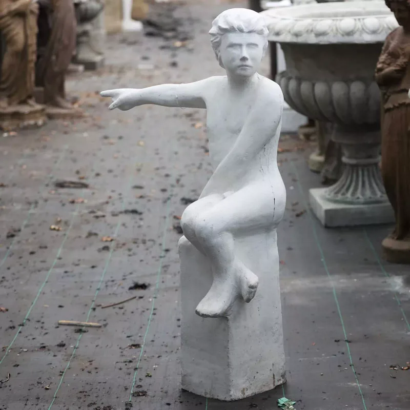 A sculpture depicting a boy seated on a rectangular plinth pointing the way The sculpture in composite resin with white painted finish