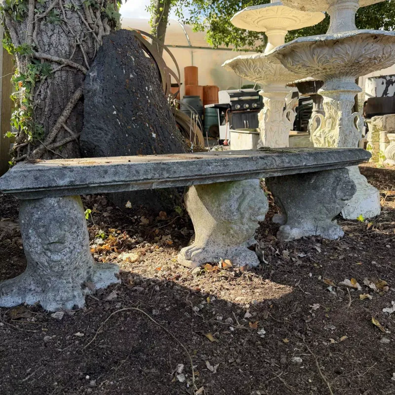 A curving garden bench or seat with three decorative supports The cast reconstituted bench with lion decoration to the supports