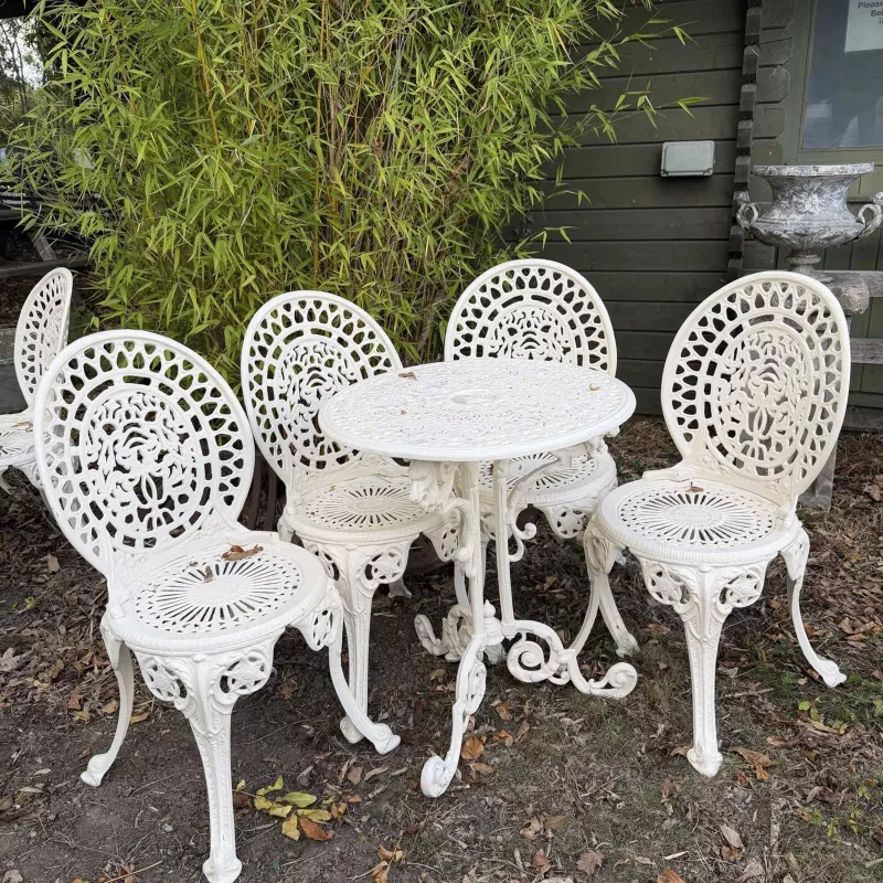 A cream painted garden table and chairs The table with pierced top and scrolling supports