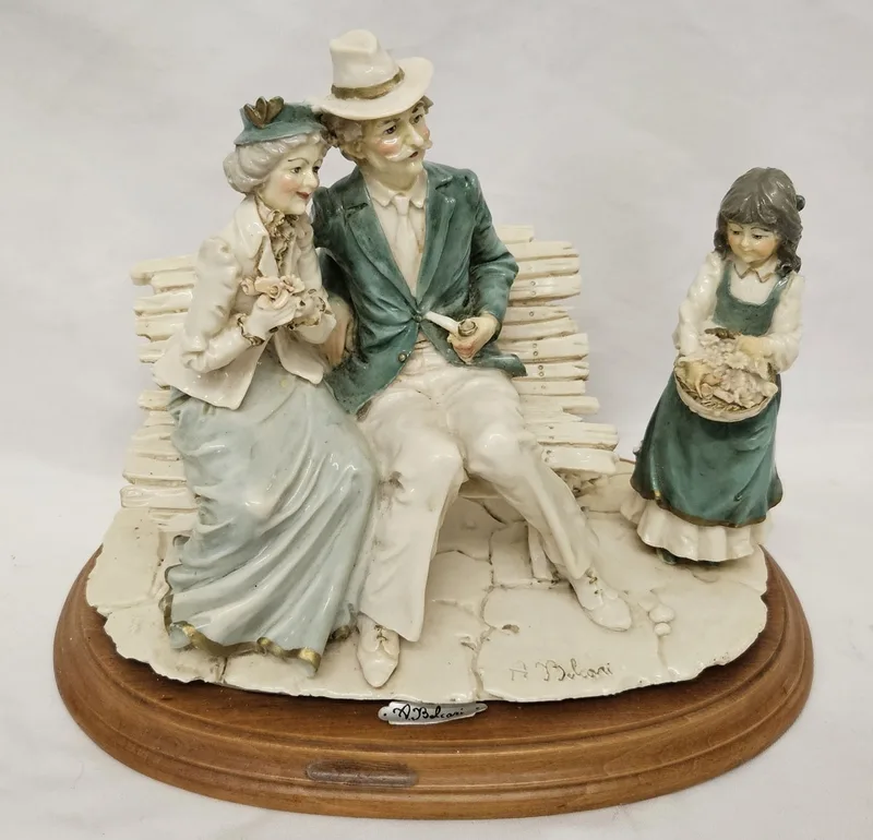 Auro Belcari Figurine Elderly Lady & Gent sat on a bench with young girl with a flower basket,