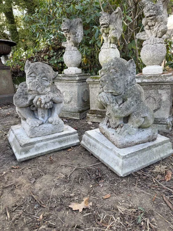 A pair of gate post finials in the form of creatures with large jowls One creature seated supporting a sword, the other a shield