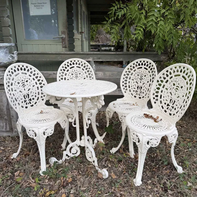 A cream painted garden table and chairs The table with pierced top and scrolling supports