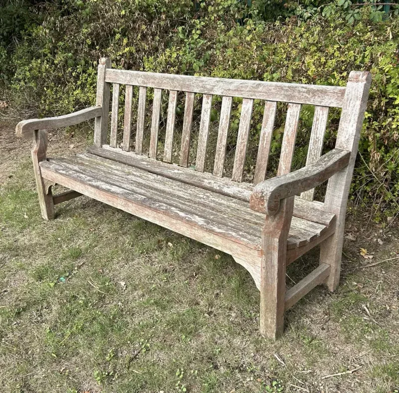 A teak garden bench by R A Lister The bench with slatted back and seat and scrolling arms