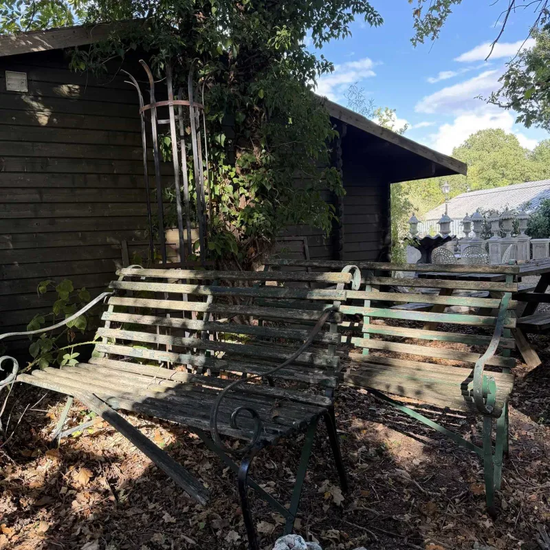 A pair of wrought iron garden benches The scrolling ends united by green painted wooden slats