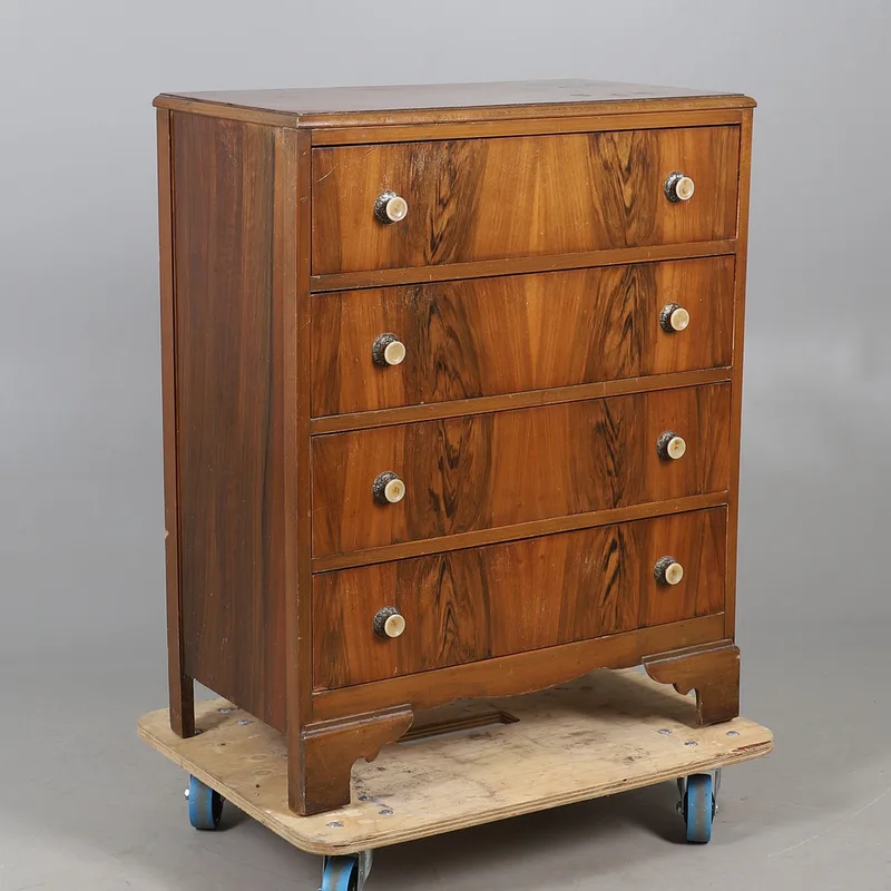 A walnut veneered chest of four drawers, with decorative simulated ivorine handles, and raised on bracket front supports.