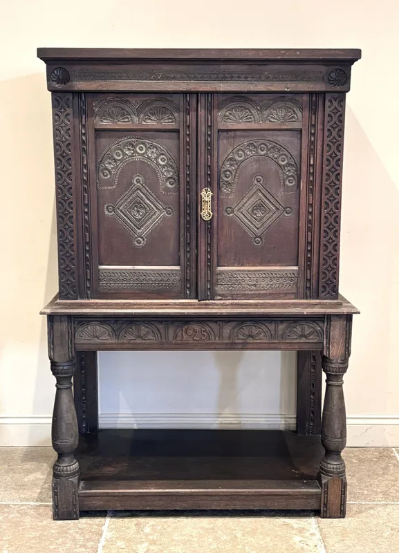 A 17th century style carved oak cabinet on stand, the upper section formed with two cupboard doors, enclosing three shelves
