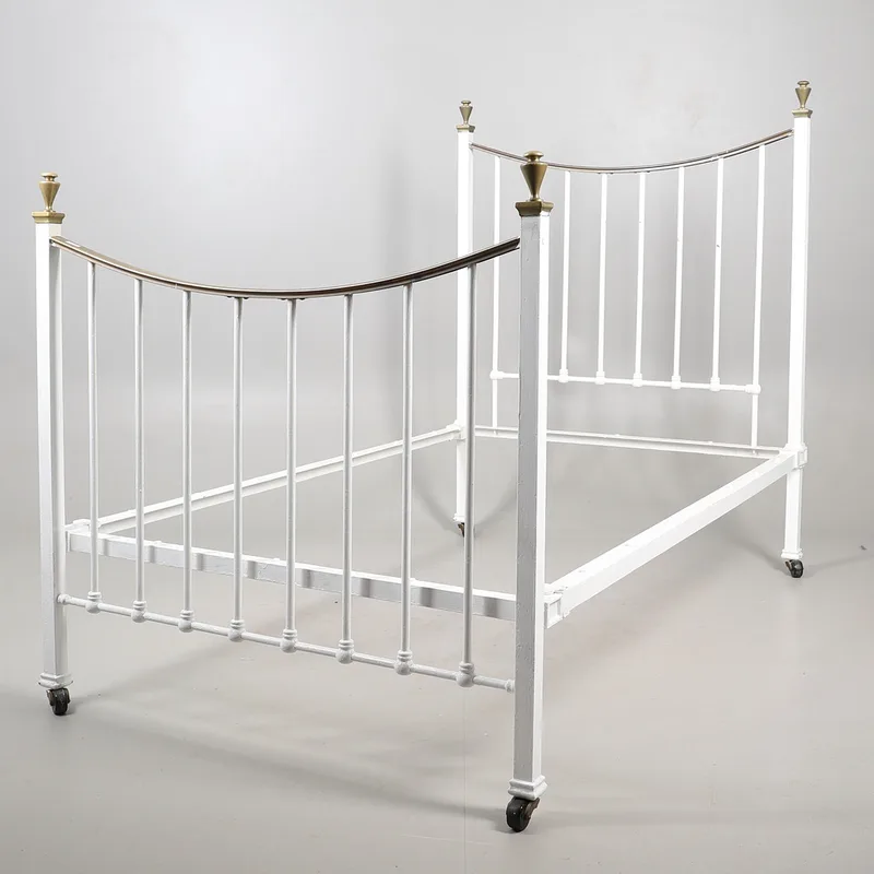 A painted iron and brass bed, with a curved head and foot board with painted spindles, raised on square supports and casters,
