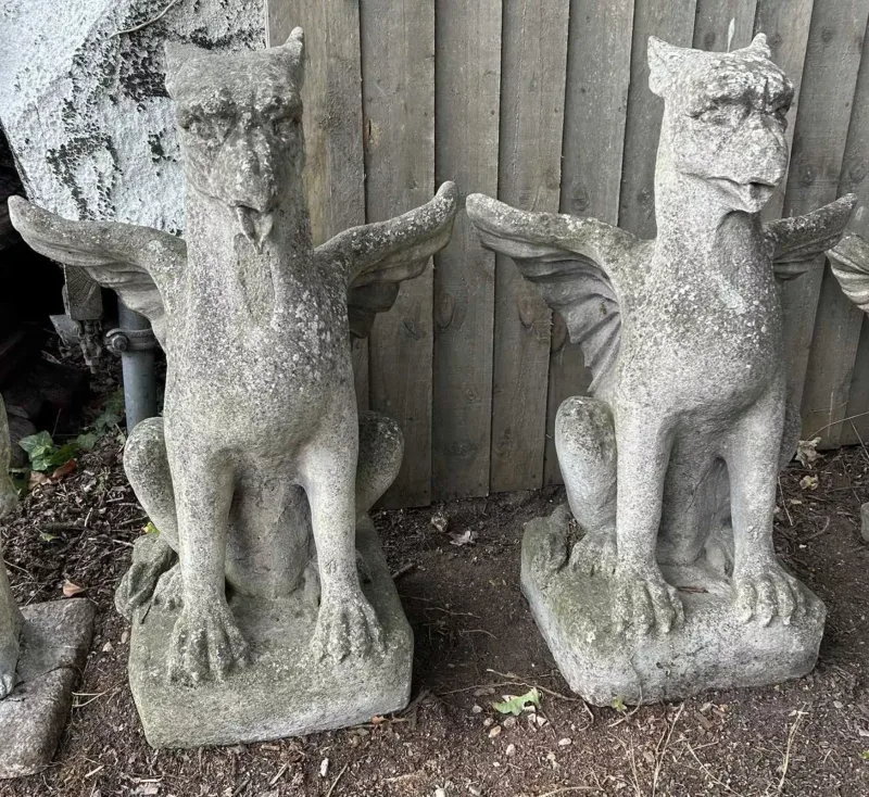 A pair of cast reconstituted stone griffins Each griffin with tongue protruding from its beak and with spread wings and seated on its haunches
