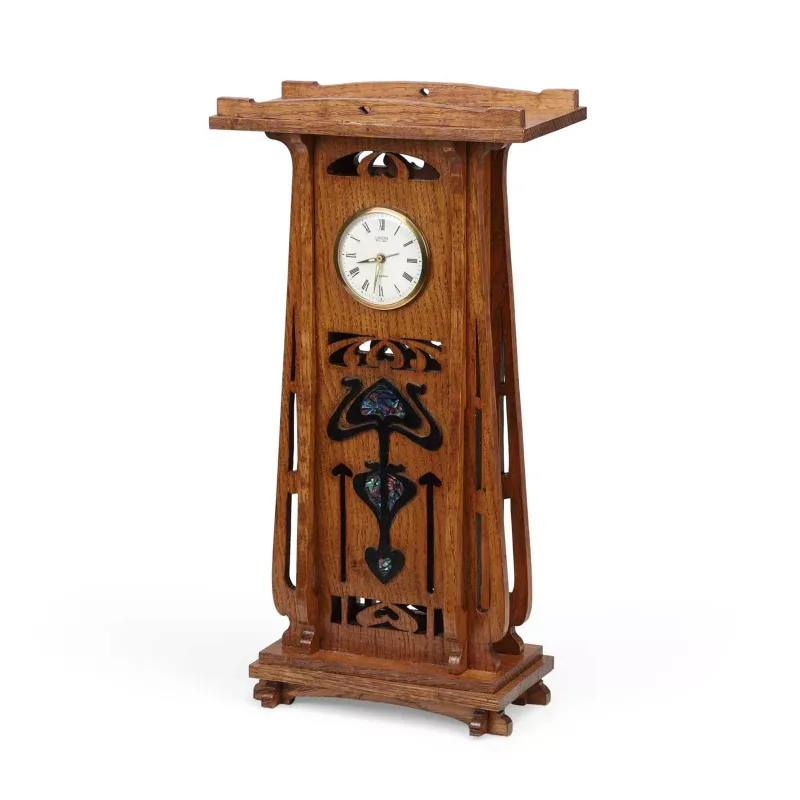 An Oak Mantel Clock In The Art Nouveau Taste the shaped and overhanging top above a tapering case, the frieze pierced with a stylised heart and scrolls